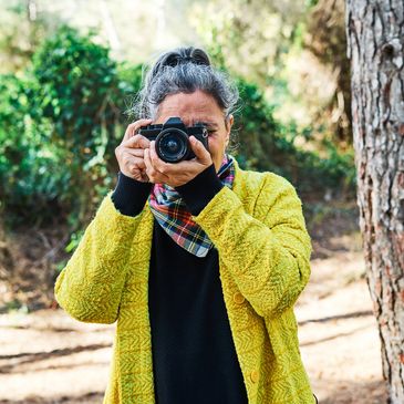 Woman in yellow coat taking a photo with a camera outdoors.