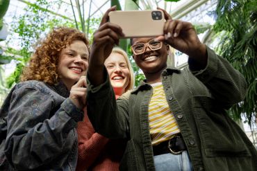 Three friends smiling and taking a selfie together outdoors.