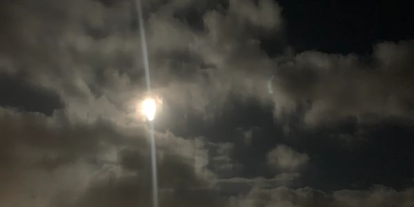 Bright moon shining through cloudy night sky.