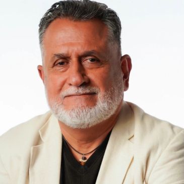Hombre mayor con barba canosa y chaqueta clara.