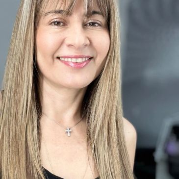 Mujer sonriente con cabello largo y collar de cruz.