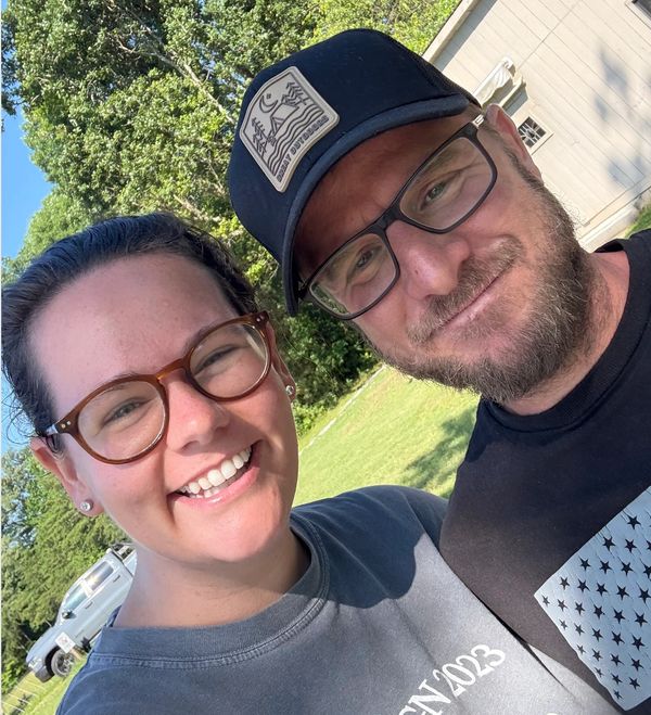 Smiling couple outdoors on a sunny day, wearing glasses.