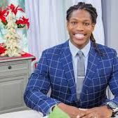 Smiling man in a blue checkered suit sitting at a desk.