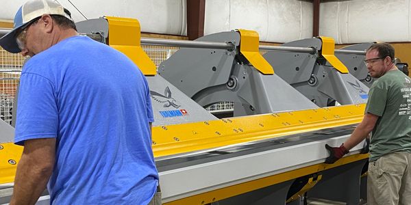 Two men operating a large industrial sheet metal bending machine.