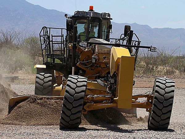 A yellow grader machine leveling gravel on a construction site.