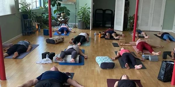 Group practicing relaxation yoga pose in a calm, plant-filled studio.
