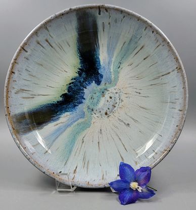 Round ceramic plate with blue and black glaze, accompanied by a purple flower.