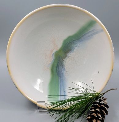 White ceramic plate with abstract green and blue design, displayed with pine cone and pine needles.