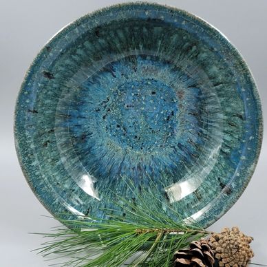 Ceramic plate with blue-green glaze and pine cone decoration.