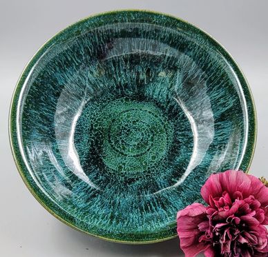 A glossy green and blue ceramic bowl with a pink flower beside it.