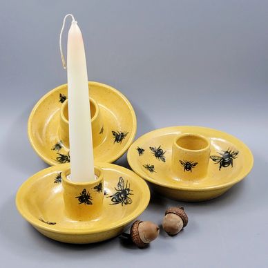 Yellow ceramic candle holders with black bee designs and a white candle.