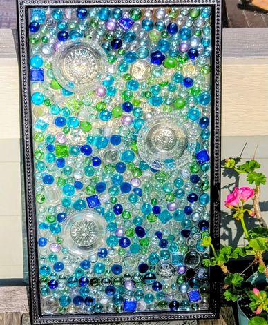Colorful glass marbles and bowls arranged in a framed mosaic artwork.