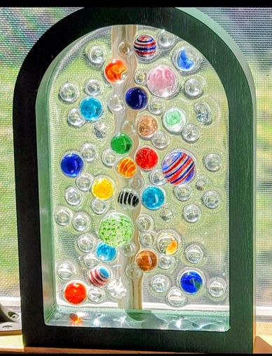 Colorful glass marbles arranged in a decorative frame with sunlight shining through.