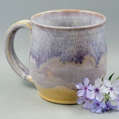 Handcrafted ceramic mug with purple glaze and delicate flowers beside it.