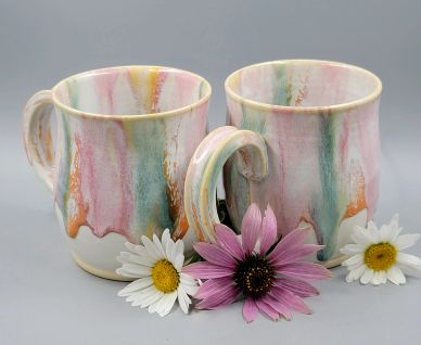 Two colorful ceramic mugs with floral designs and fresh flowers.