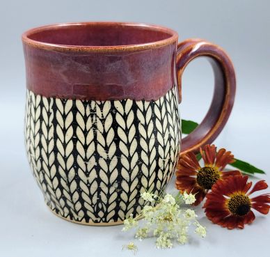 Handcrafted ceramic mug with intricate leaf pattern and reddish-brown glaze.