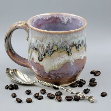 Artisan ceramic coffee mug with coffee beans and ornate silver spoon.