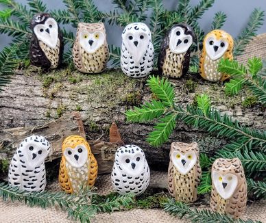 Ten small ceramic owls displayed on a log with green foliage.
