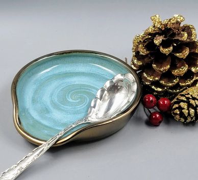 Decorative spoon rest with a turquoise swirl pattern and holiday pinecones.