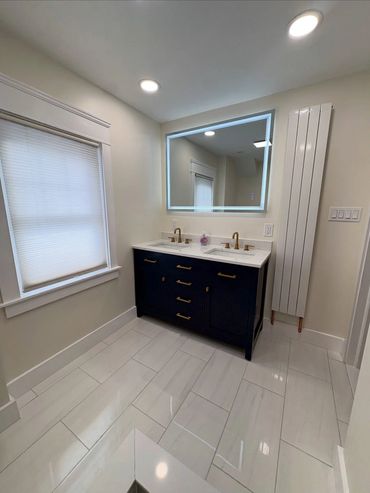 Modern bathroom with navy vanity, illuminated mirror, and white tiled floor.