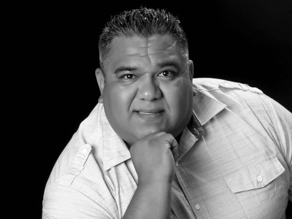 Man posing thoughtfully with hand on chin against black background.
