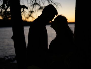 Silhouetted couple sharing a tender moment at sunset by the water.