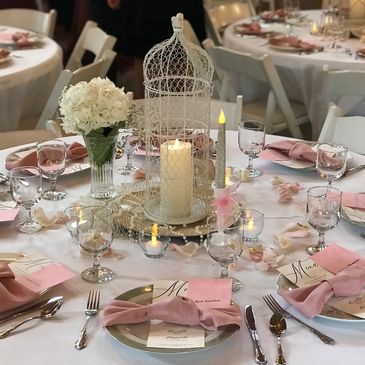 Elegant wedding table setting with pink napkins and a birdcage centerpiece.