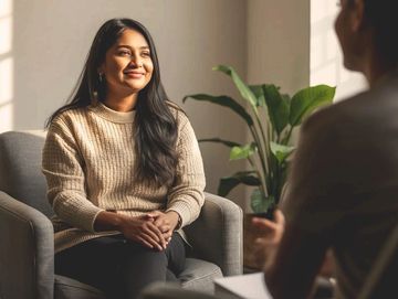 Woman in beige sweater smiling during a conversation indoors.