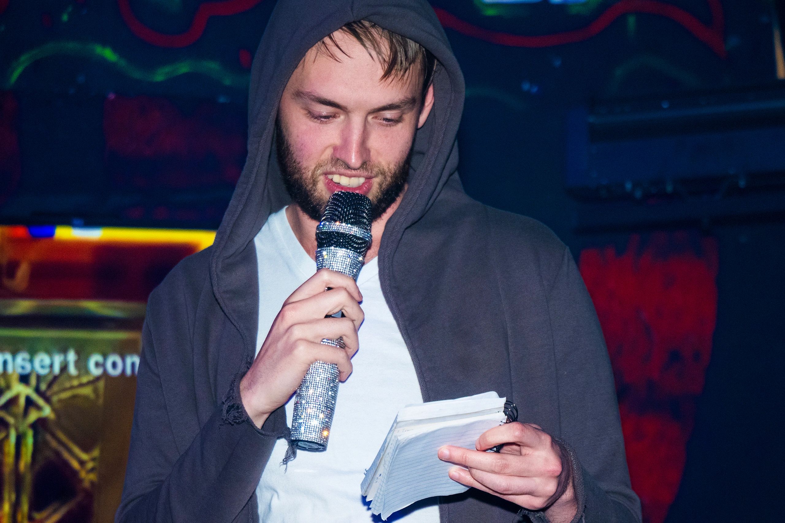 Man in hoodie holding a sparkling microphone and reading notes.