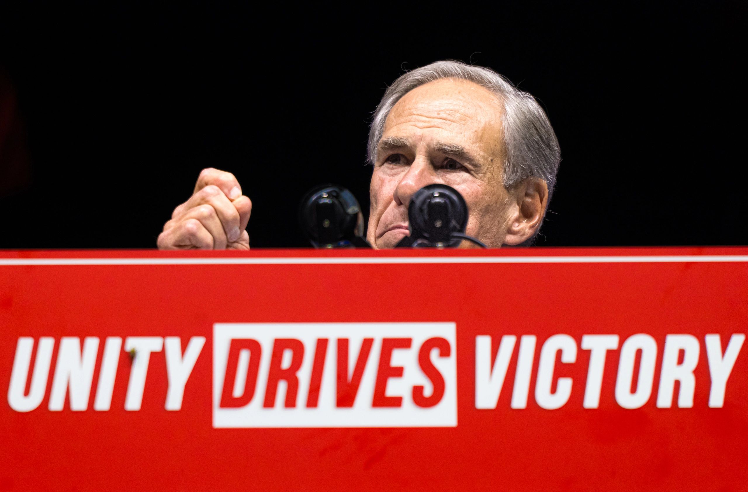 Man speaking behind a red podium with the message "UNITY DRIVES VICTORY".