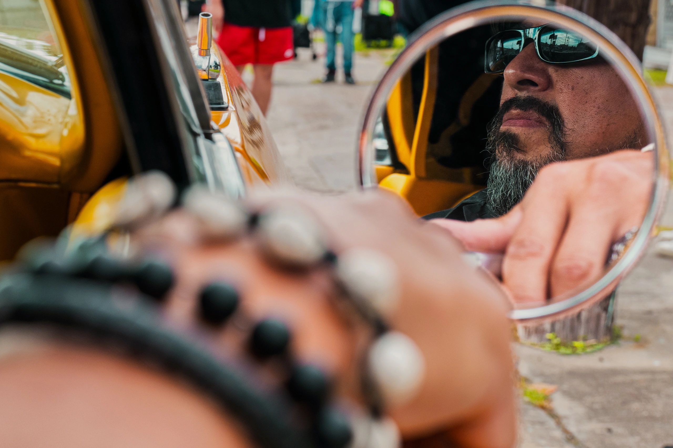 Reflection of a man with sunglasses in a car's side mirror.