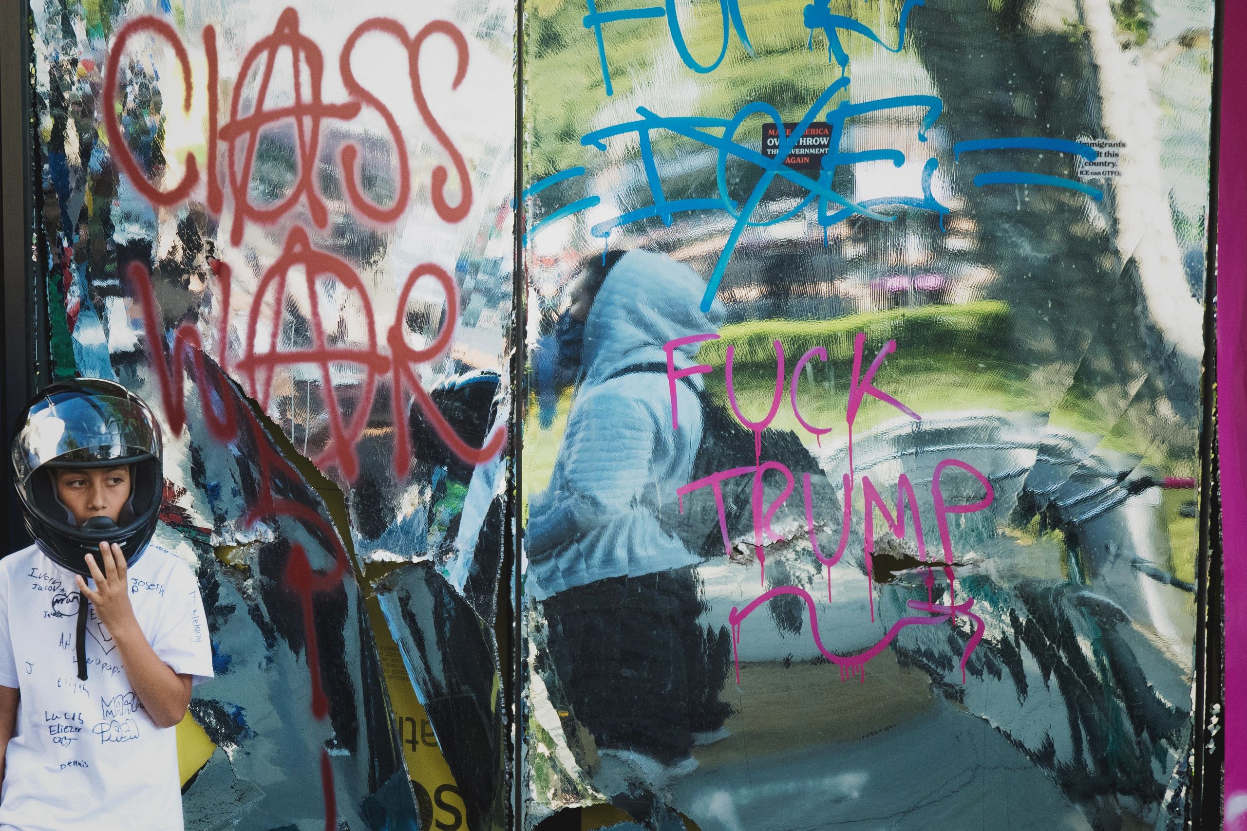 A young person in a helmet stands near a wall covered in political graffiti.