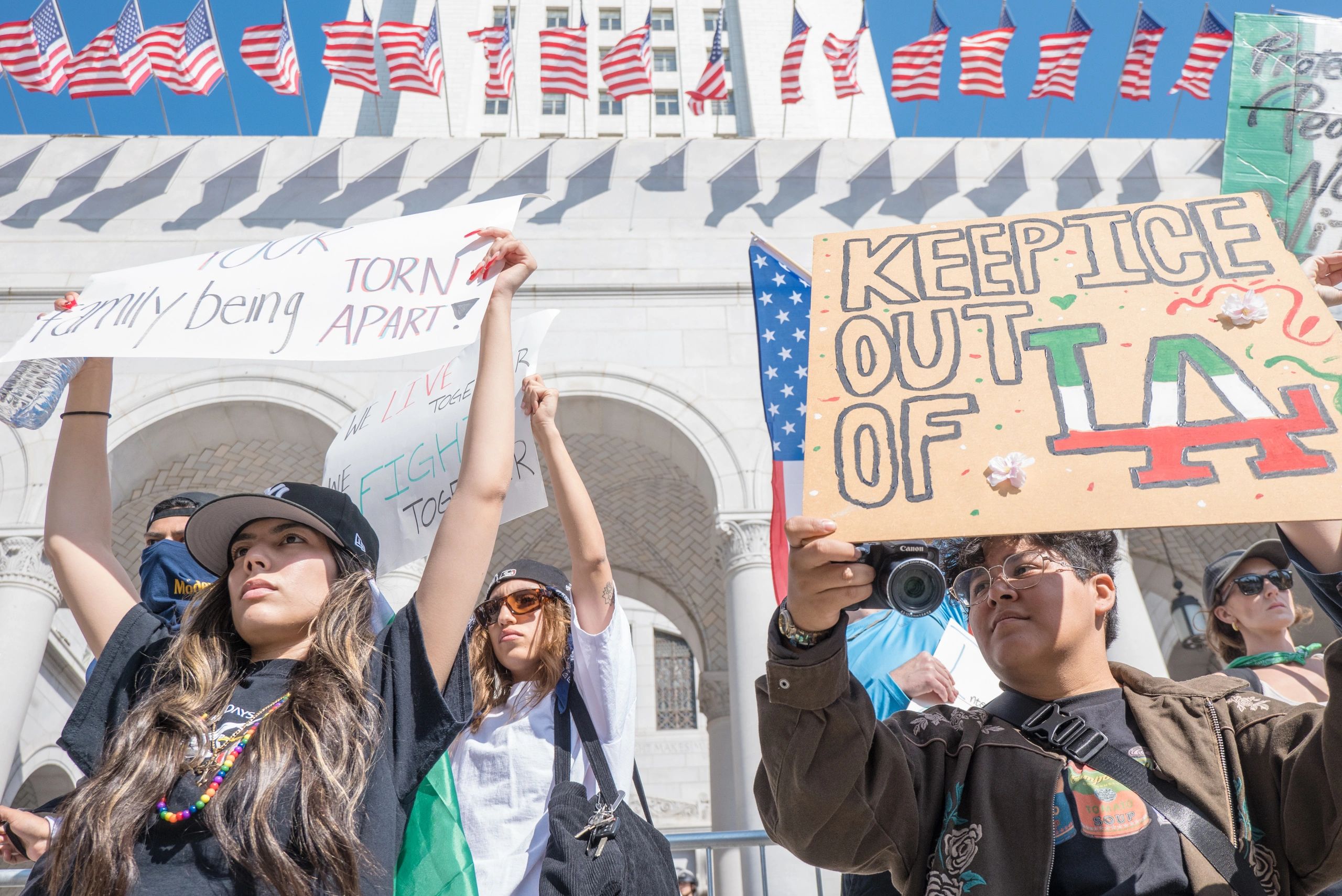Protesters hold signs advocating against ICE policies, standing strong under American flags.