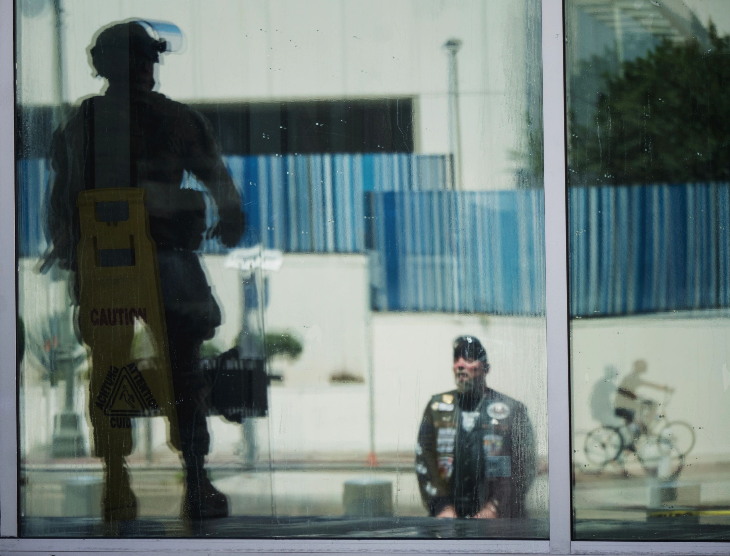 Reflections of a soldier and a man on a bike seen through a dirty glass window.