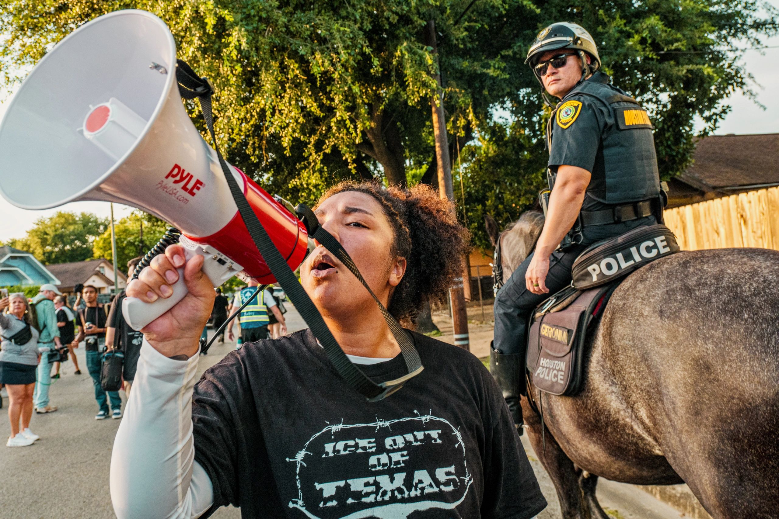 Person shouting through megaphone near mounted police officer.