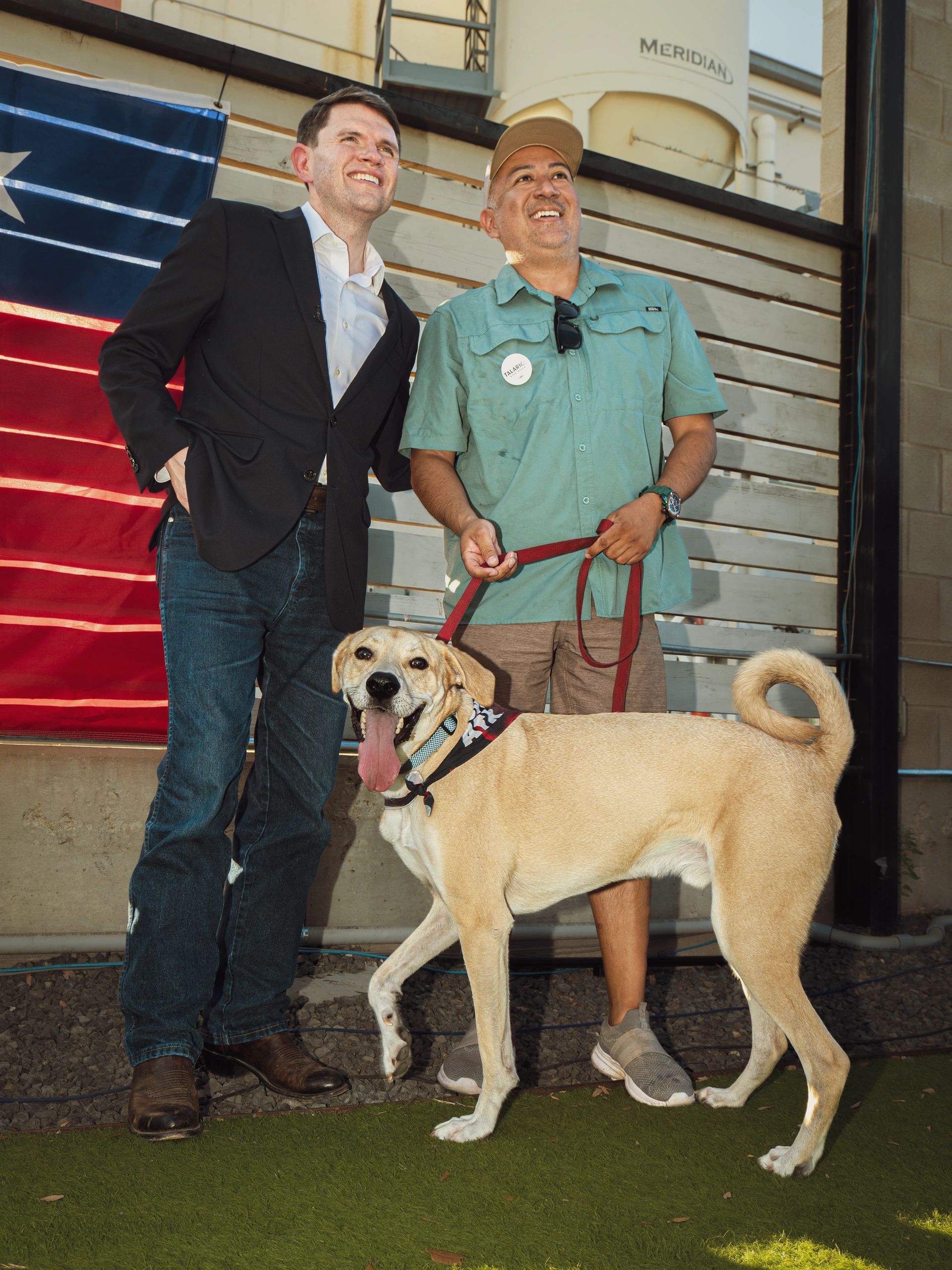 Two men smiling with a happy dog on a leash.