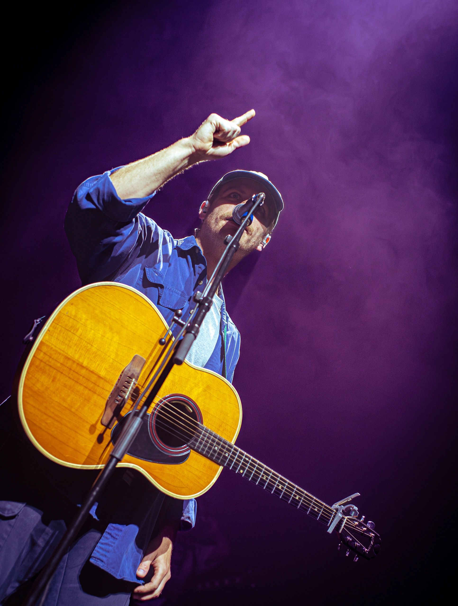 Musician with a guitar performing on stage under purple lights.