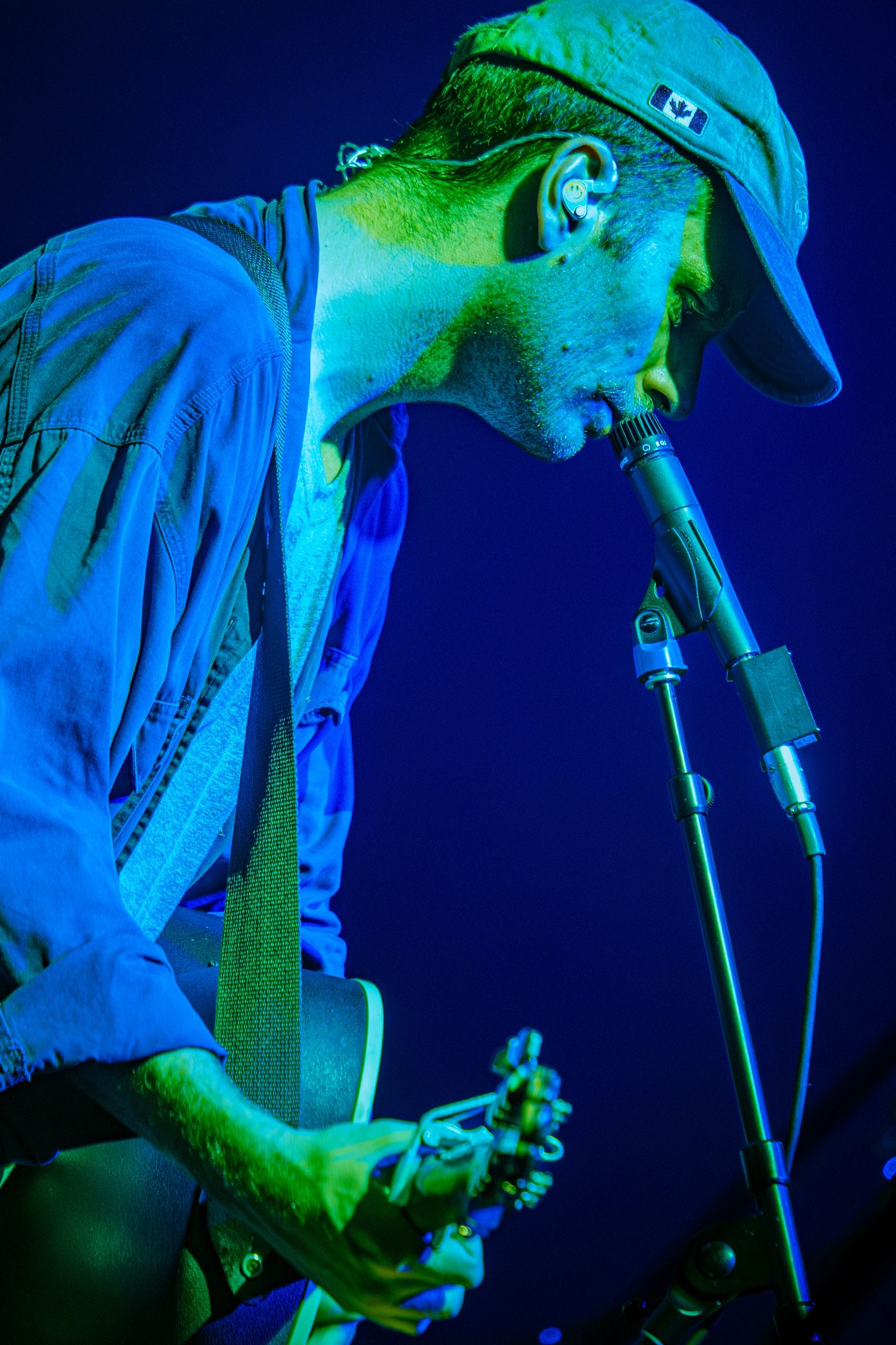 Musician passionately singing and playing guitar under blue-green stage lights.