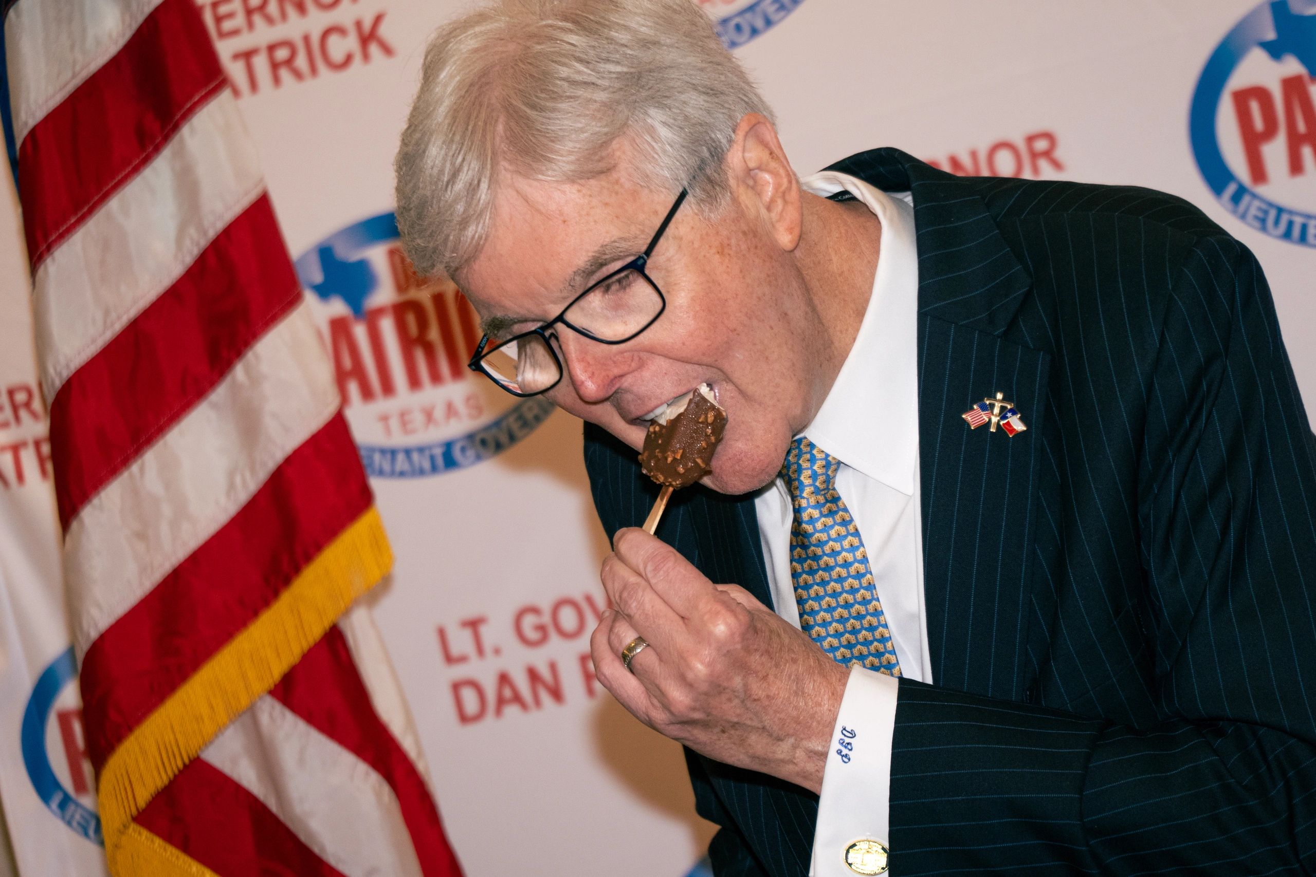 Man in suit eating chocolate-covered ice cream bar at political event.