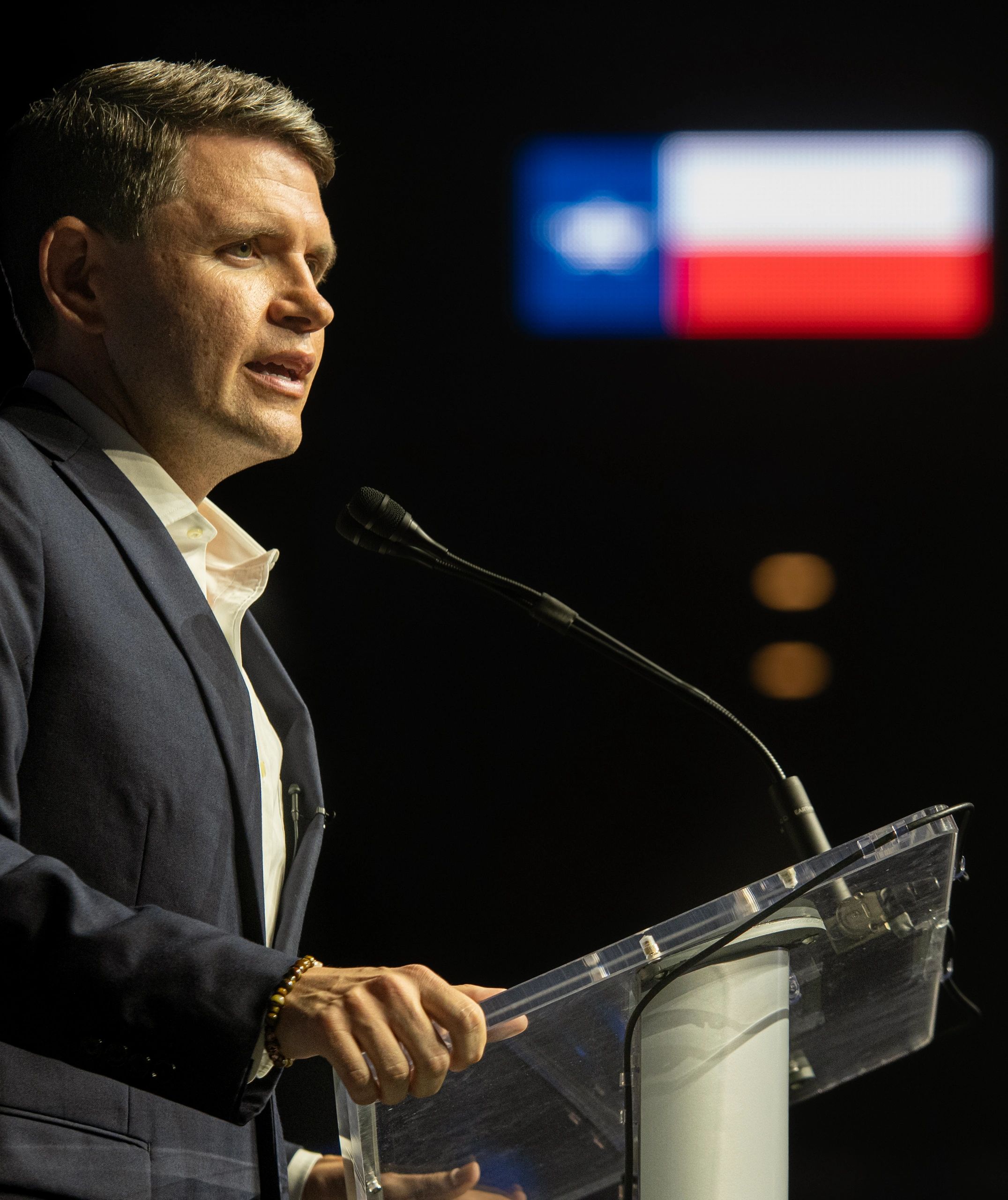 Man speaking at podium with Texas flag in background.