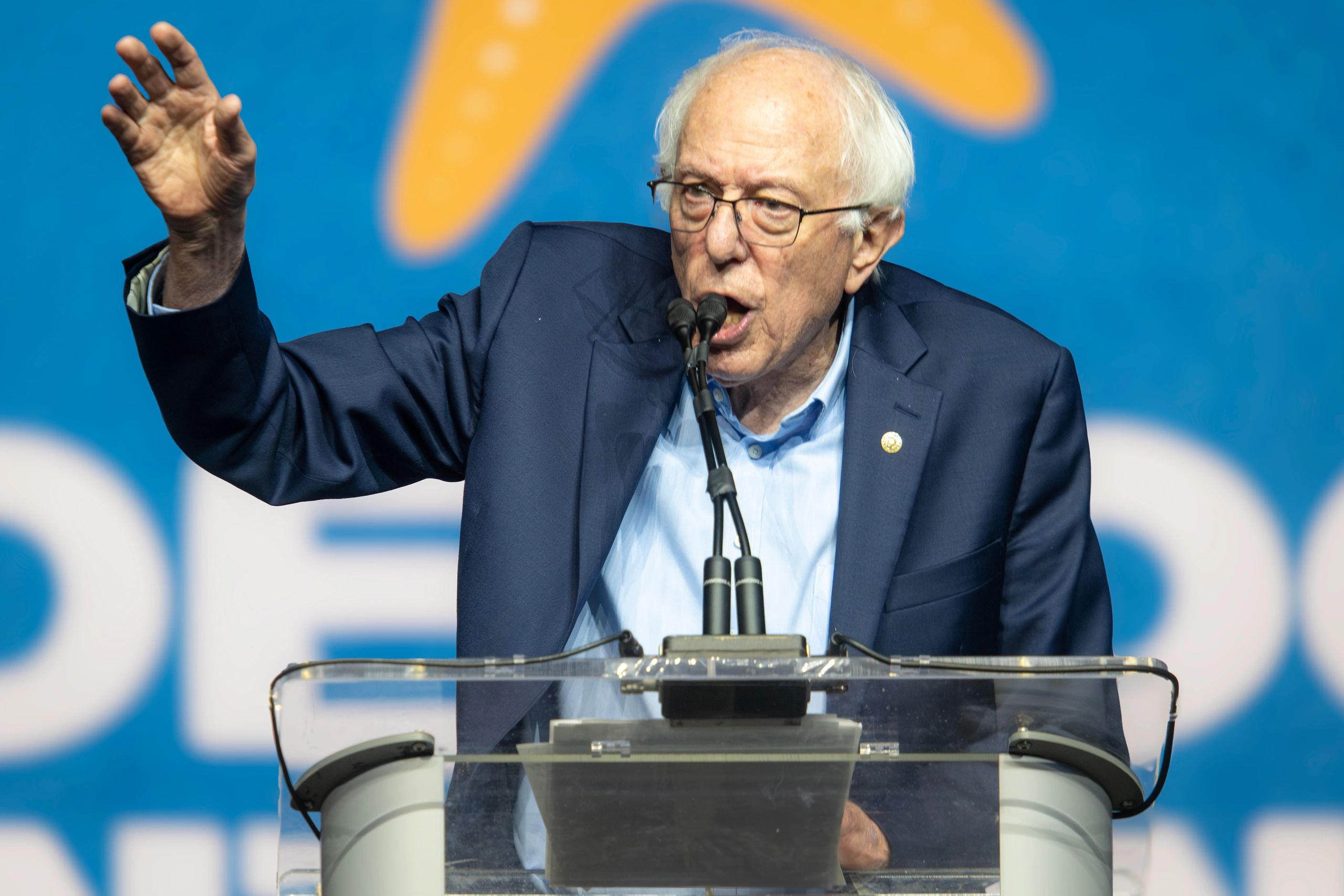 Elderly man passionately speaking at a podium with microphones.