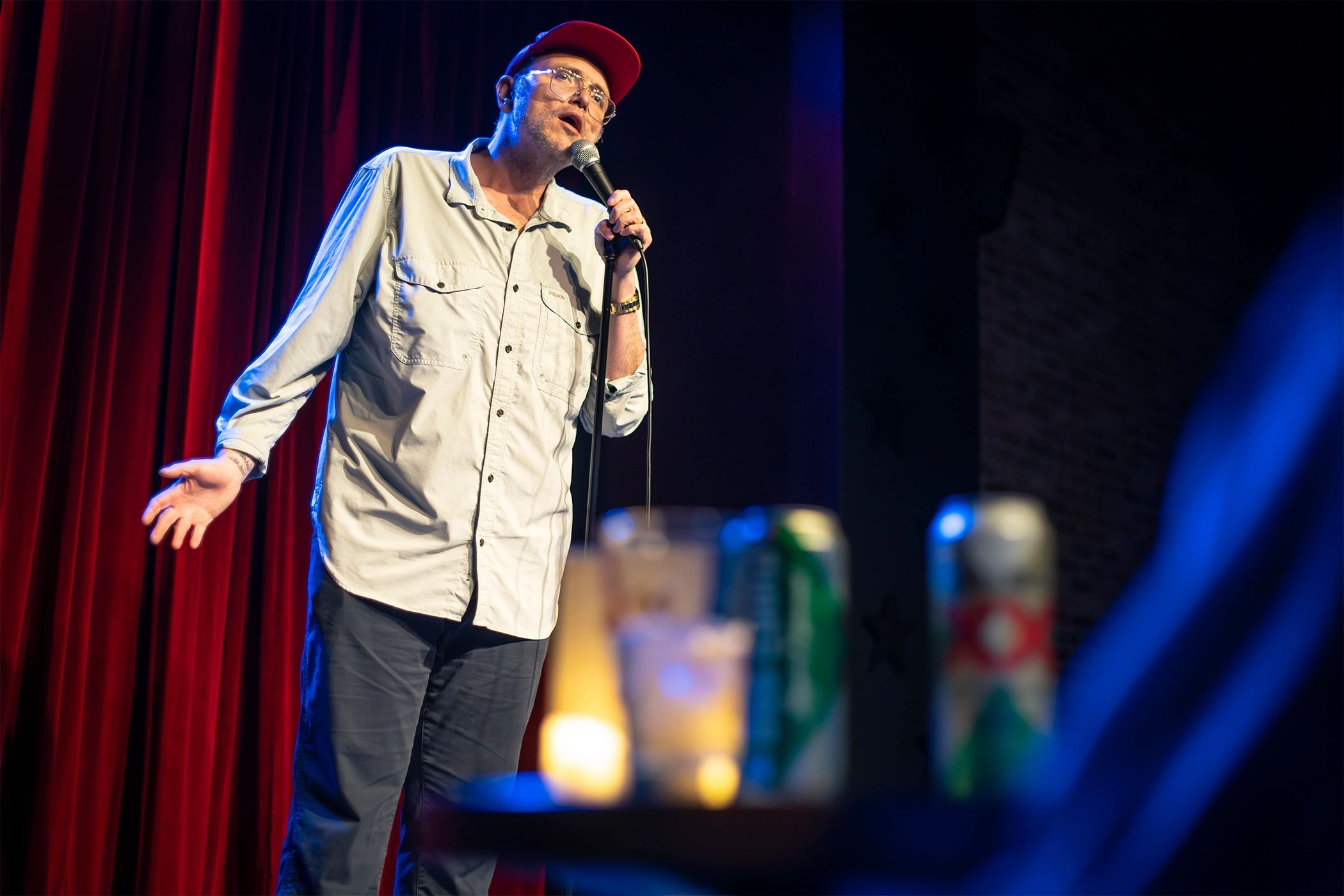 Comedian performing stand-up on stage with red curtains.