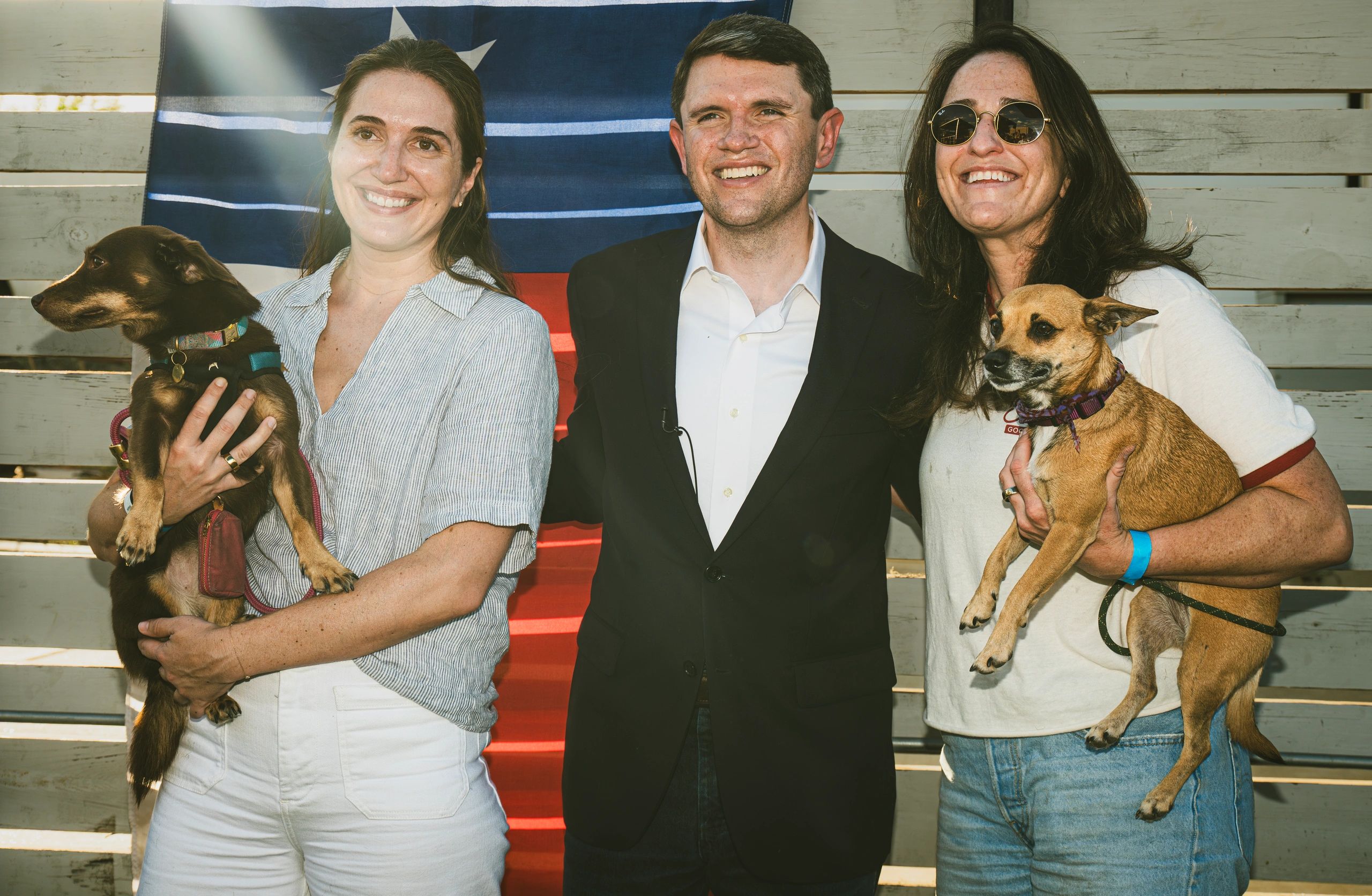 Three people smiling with two dogs in their arms.