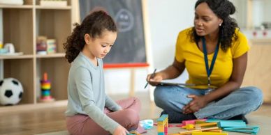 Child playing with blocks while teacher observes and takes notes.
