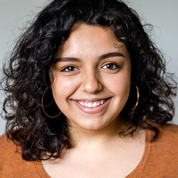 Smiling woman with curly hair and hoop earrings in an orange top.