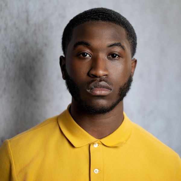 Portrait of a young man in a yellow polo shirt with a neutral expression.