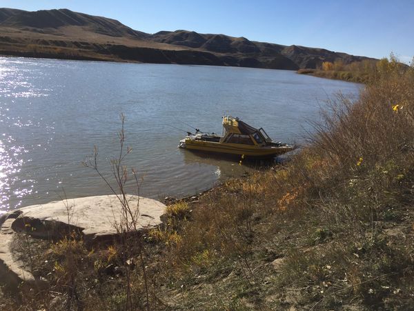 A small yellow boat docked by a riverbank with hills in the background.