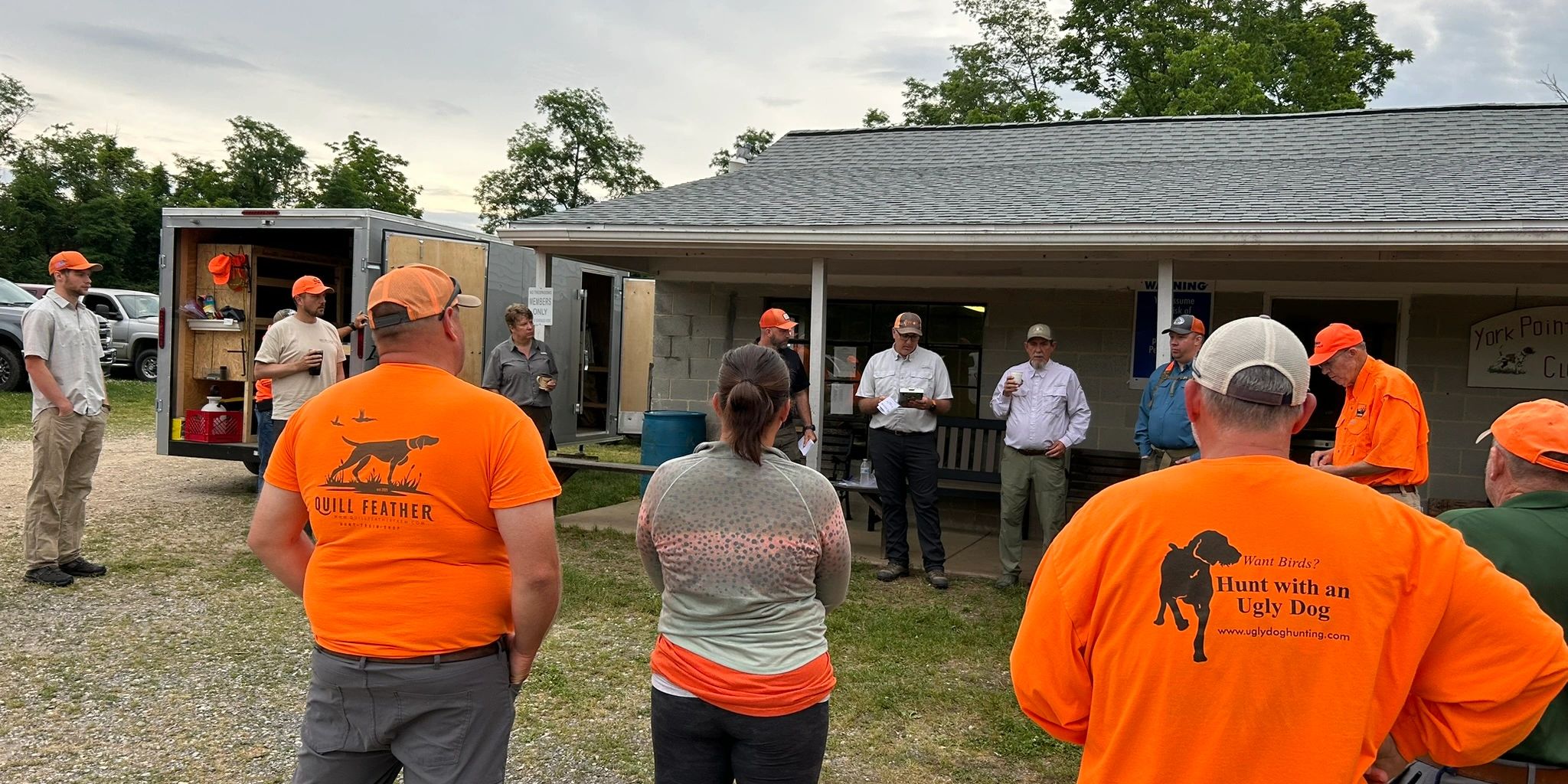 A group of people gathered outdoors wearing bright orange hunting gear.