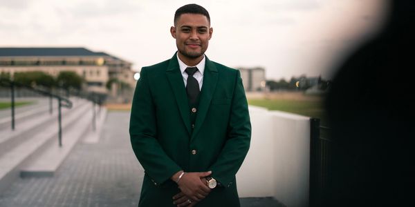 Man in a green suit smiling outside near stairs.