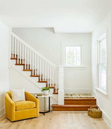 Cozy yellow chair beside wooden stairs in bright room.